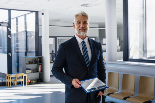 Confident senior manager holding documents in modern clinic or office environment.