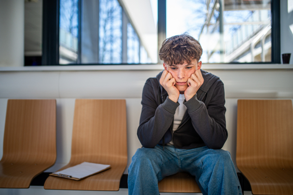 Teenage boy waiting alone in hospital waiting area before preventive medical checkup.