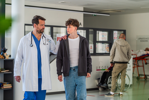 Doctor walking with teenage patient after successful checkup or medical procedure in hospital hallway.