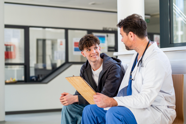 Teenage boy smiling talking with supporting doctor, receiving positive health news.