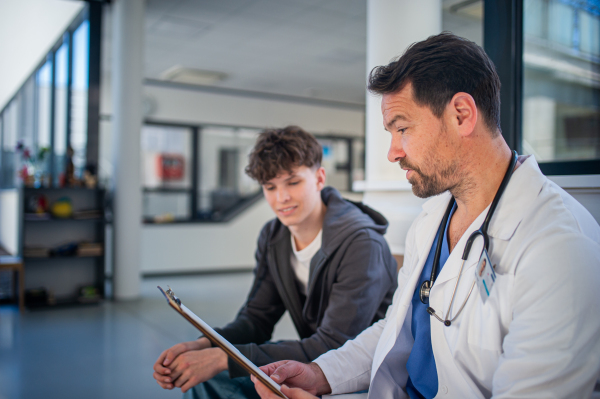 Doctor explaining medical procedure to teenage patient in hospital waiting room. Medical setting.