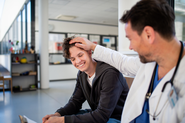Teenage boy smiling talking with supporting doctor, receiving positive health news.