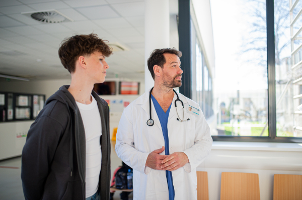 Doctor walking teenage patient out from modern medical clinic, hospital.