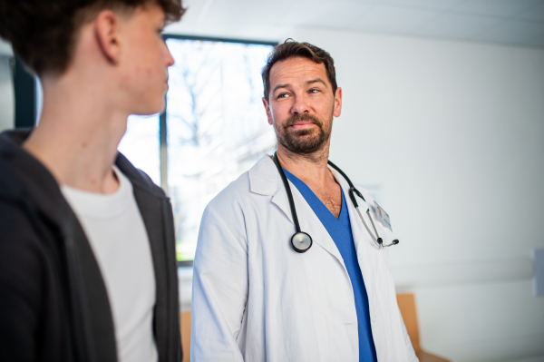 Doctor walking with teenage patient after successful checkup or medical procedure in hospital hallway.