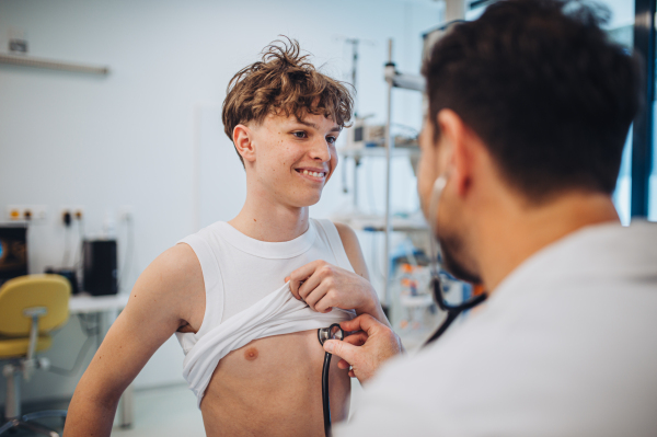 Teen boy undergoing medical checkup with smiling doctor in hospital room.
