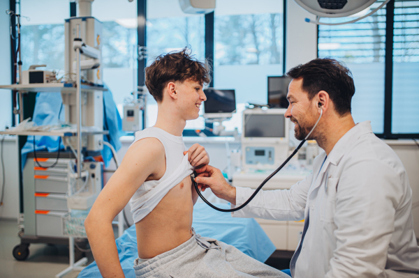 Teen boy undergoing medical checkup with smiling doctor in hospital room.