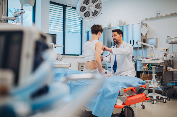 Teen boy undergoing medical checkup with smiling doctor in hospital room.