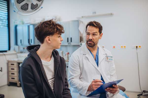 Close-up of doctor and teenage patient filling out mental health evaluation form together.