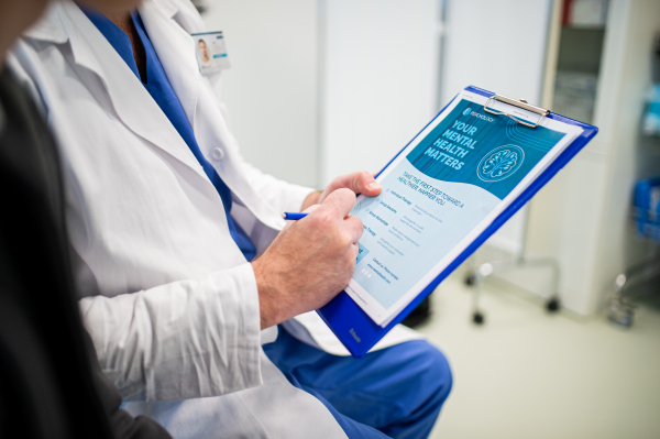 Close-up of doctor and teenage patient filling out mental health evaluation form together.