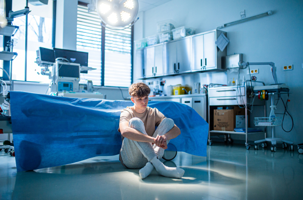Worried teenage patient sitting alone on hospital floor, struggling with mental health issues and anxiety.