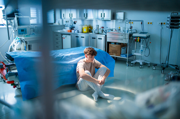Teenage boy sitting depressed on hospital floor, struggling with mental health issues and anxiety.