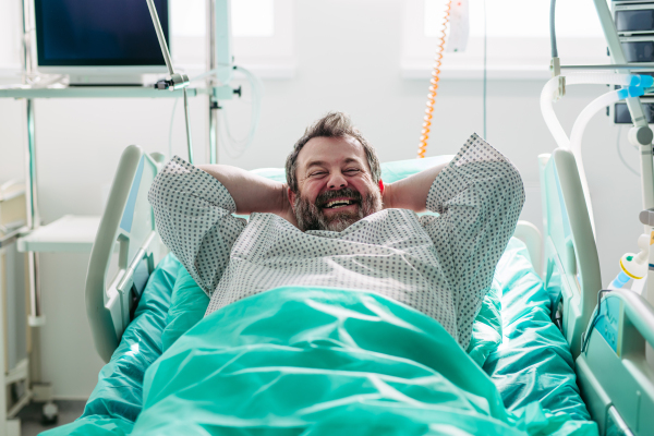 Patient resting in hospital bed with hands behind head.