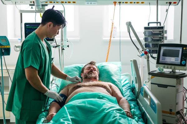 Doctor placing ECG electrodes on male patient in hospital bed