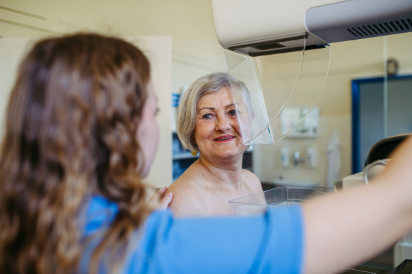 Nurse adjusts elderly patient for accurate breast imaging. Preventive breast cancer screening.
