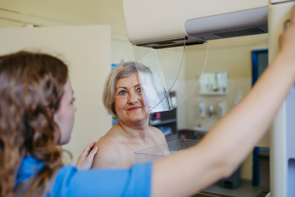 Nurse adjusts elderly patient for accurate breast imaging. Preventive breast cancer screening.