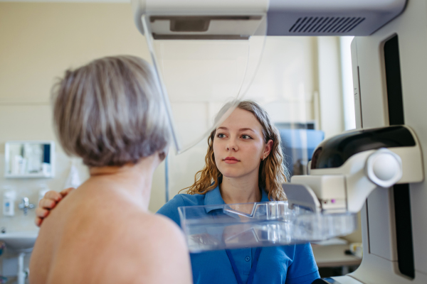 Nurse adjusts older patient for accurate breast imaging. Preventive breast cancer screening.