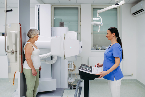 Radiologic technologist operating tilting fluoroscopy wall unit during elderly patient scan
