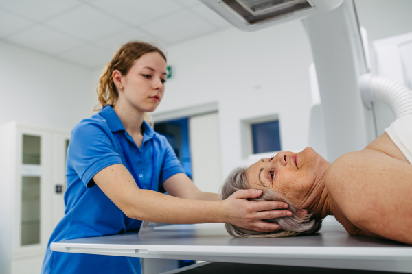 Nurse positioning elderly patient on tilting fluoroscopy table for X-ray scan