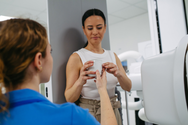 Young woman preparing for dynamic X-ray on tilting fluoroscopy wall unit, drinking contrast liquid.