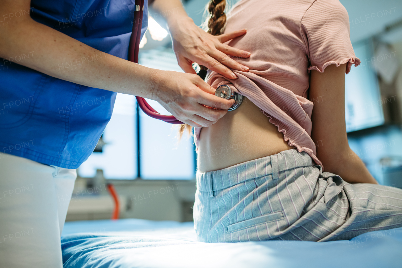 Close up of pediatrician listening to girl's breathing during routine check-up.