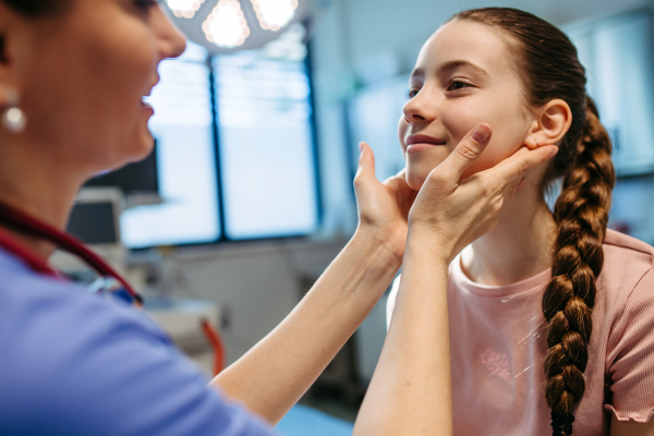 Doctor examining girl's neck for swollen lymph nodes.