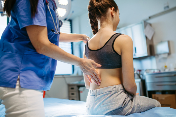 Pediatrician checking girl's spine during routine health check-up.