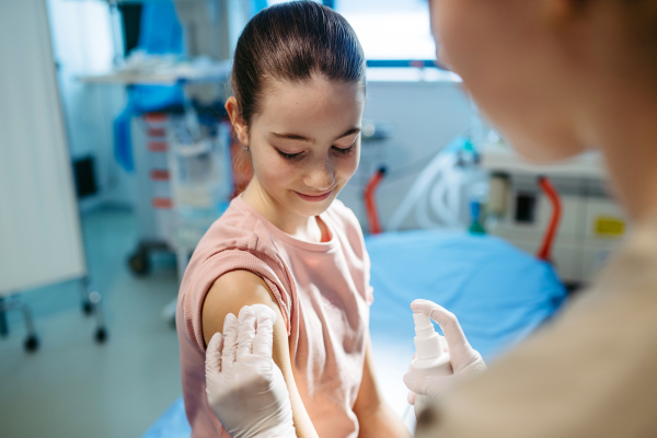 Nurse cleaning girl's skin with antiseptic in preparation for vaccination.