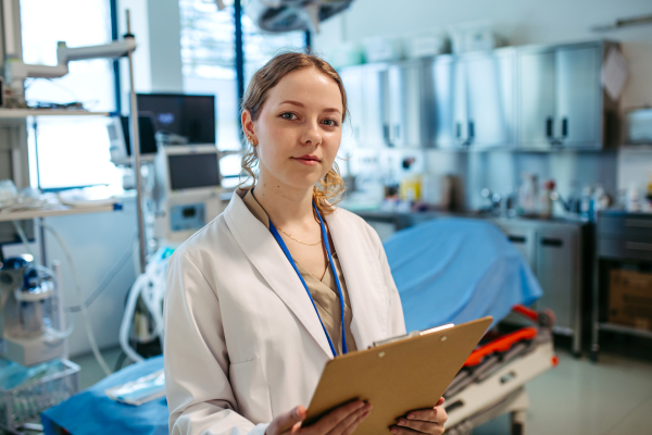 Confident young doctor holding patient chart in hospital room.