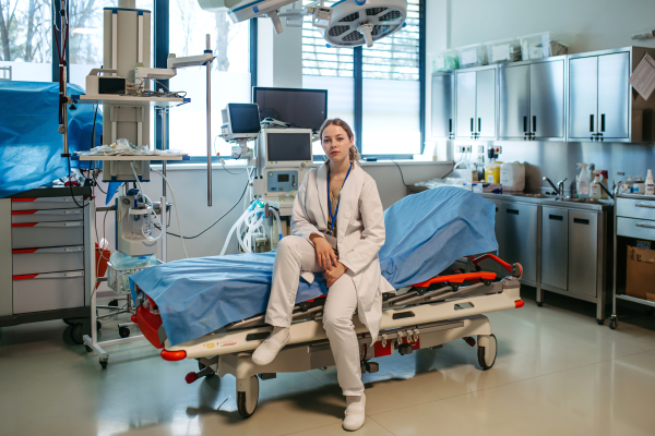 Confident young doctor sitting on examination table in emergency room.