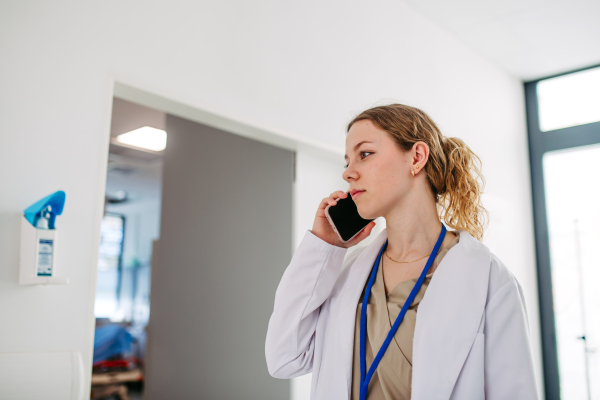 Confident young doctor making phone call in hospital hallway.