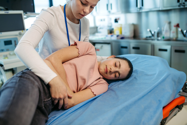 Female doctor palpating girl's abdomen in hospital.