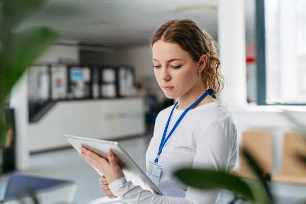 Portrait of female doctor standing in hospital hallway, reading document in tablet.