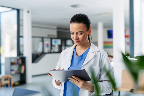 Portrait of female doctor standing in hospital hallway, reading document in tablet.