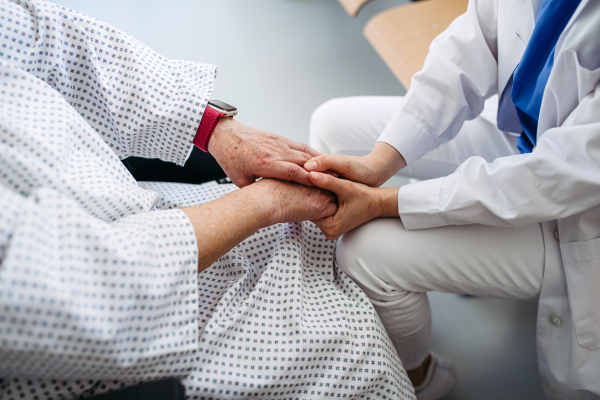 Doctor holding hands with senior patient in compassionate gesture, medical setting.