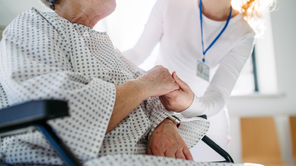 Doctor holding hands with senior patient in compassionate gesture, medical setting.
