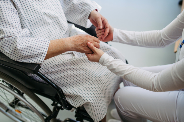 Doctor holding hands with senior patient in compassionate gesture, medical setting.