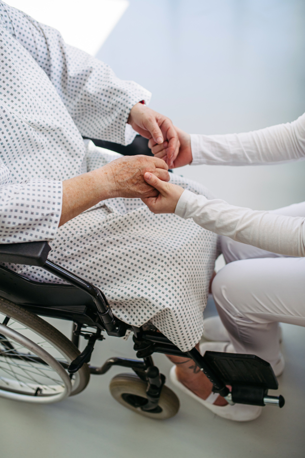 Doctor holding hands with senior patient in compassionate gesture, medical setting.