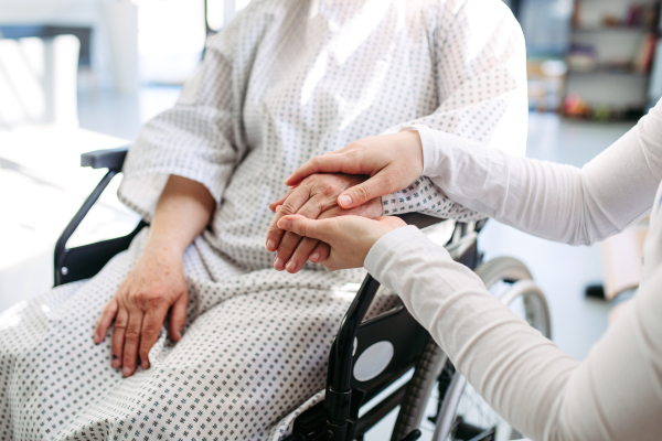 Nurse holding hand of senior patient in wheelchair