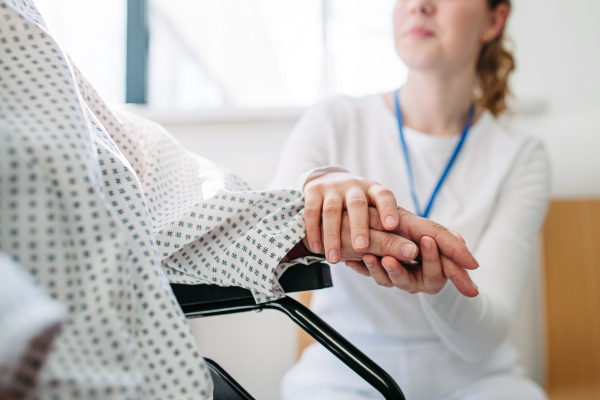 Nurse holding hand of senior patient in wheelchair