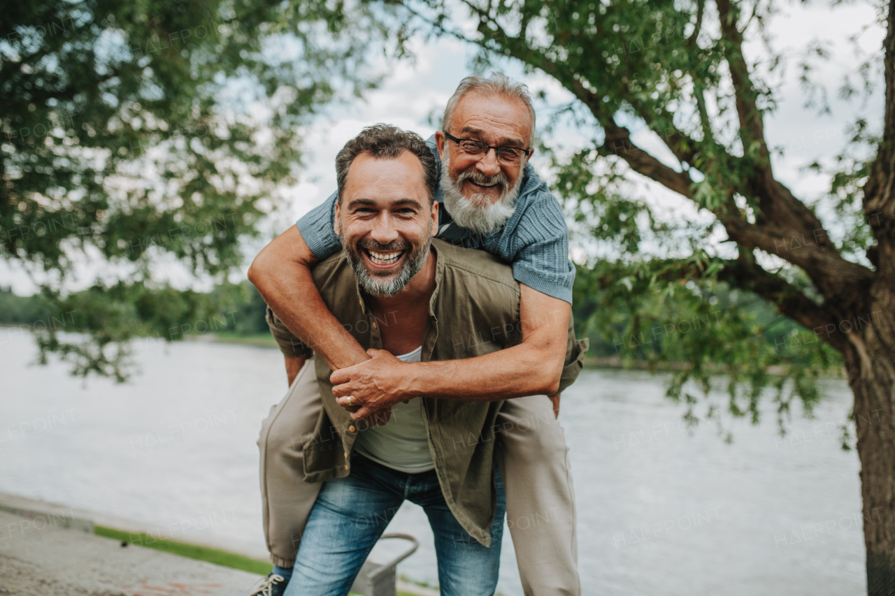 Adult son carrying older father on his back. Fathers day concept.