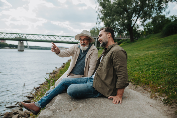 Father and adult son sharing a peaceful moment, lookign at river. Fathers day concept.