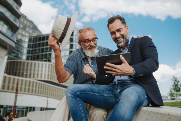 Father and adult son sharing a joyful moment, watching something in tablet. Fathers day concept.