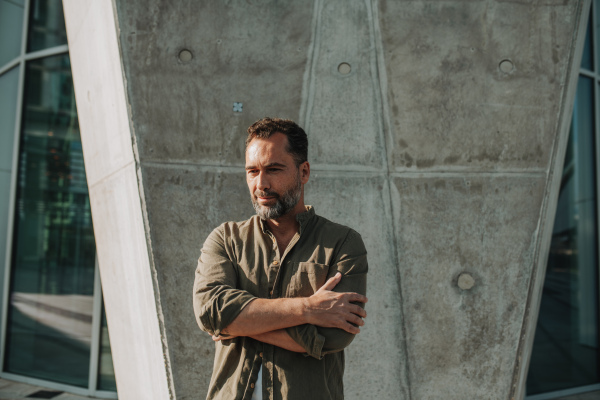 Portrait of confident middle-aged man standing outdoors by concrete wall