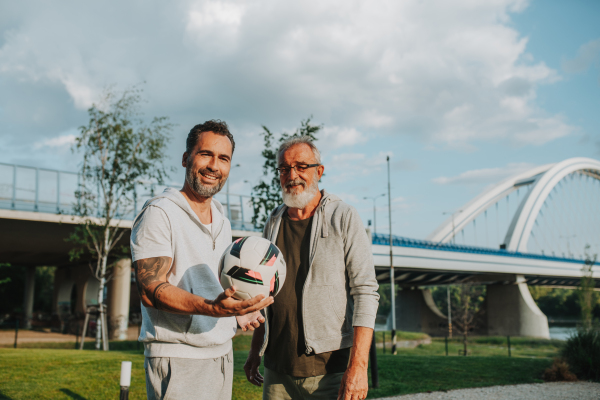 Sporty father and adult son playing football in park, throwing ball. Fathers day concept.
