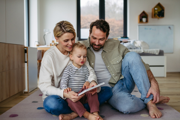 Parents reading book with little son, sitting on floor. Bonding moment.