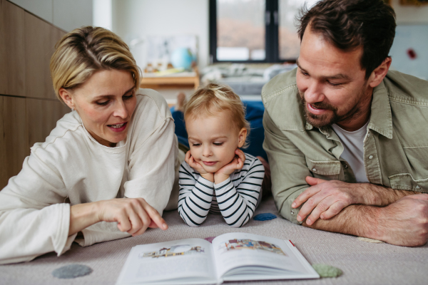 Parents reading book with little son, sitting on floor. Bonding moment.