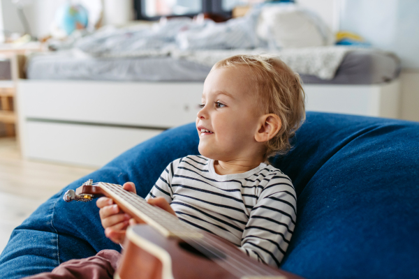 Little boy trying to play on guitar at home, having fun.