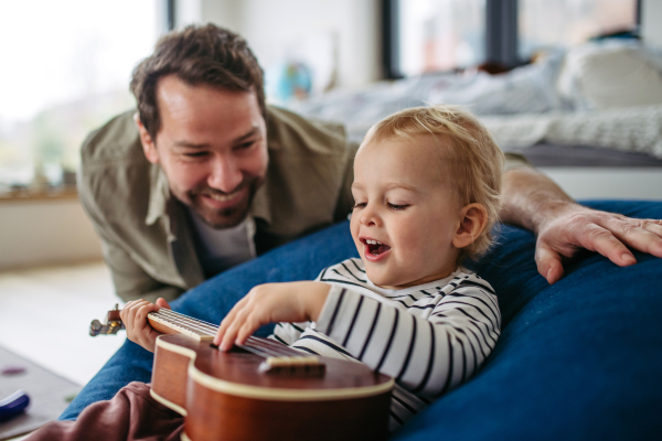 Father playing guitar with his little toddler son, having fun.