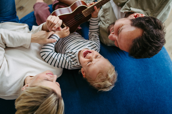 Family bonding moment. Little boy playing on guitar for his family, laughing.