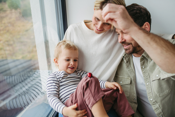 Parents playing with little son, sitting by window. Bonding moment.